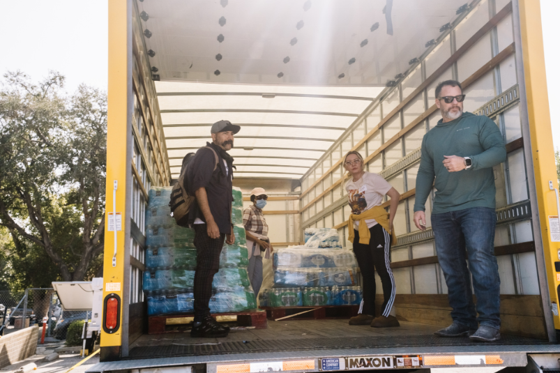 Volunteers inside a box truck with shrink-wrapped pallets of donated product, mid-unload at a Los Angeles distribution site