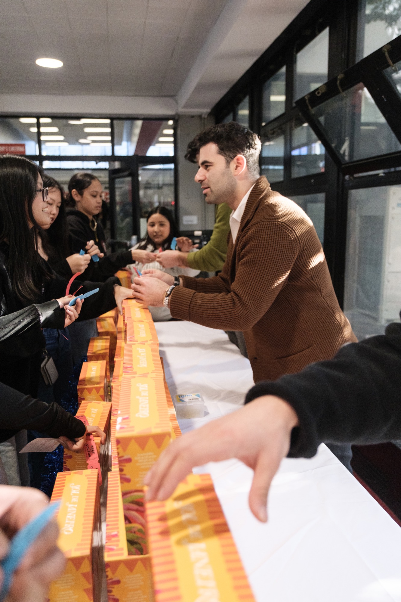 Teddy handing boxes of candy across a table to a line of kids at the holiday drive