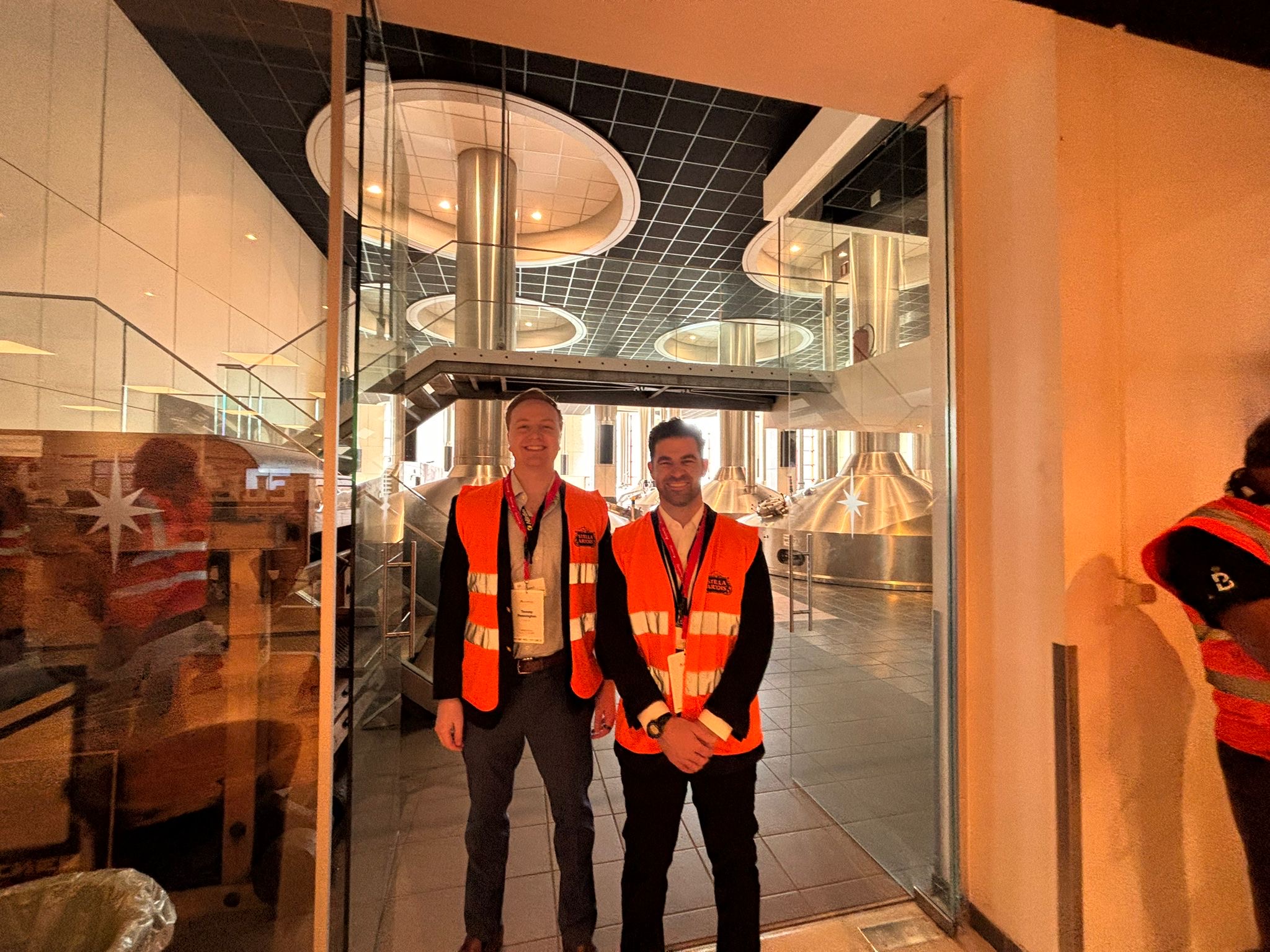 Tommy and Teddy in safety vests at the AB InBev brewery in Leuven, copper kettles behind glass